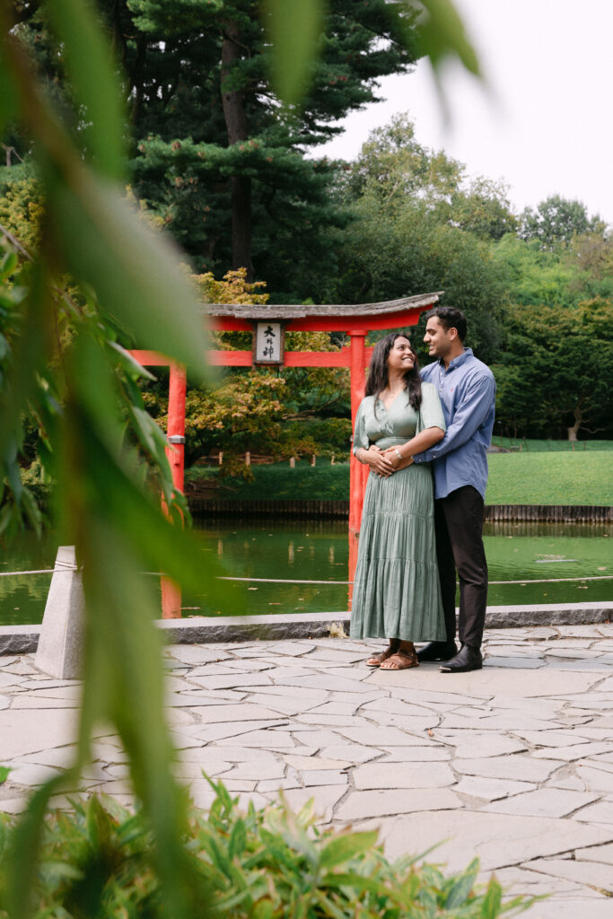 Engaged couple standing together near the Japanese torii gate at Brooklyn Botanic Garden, captured by NYC engagement and proposal photographer.
