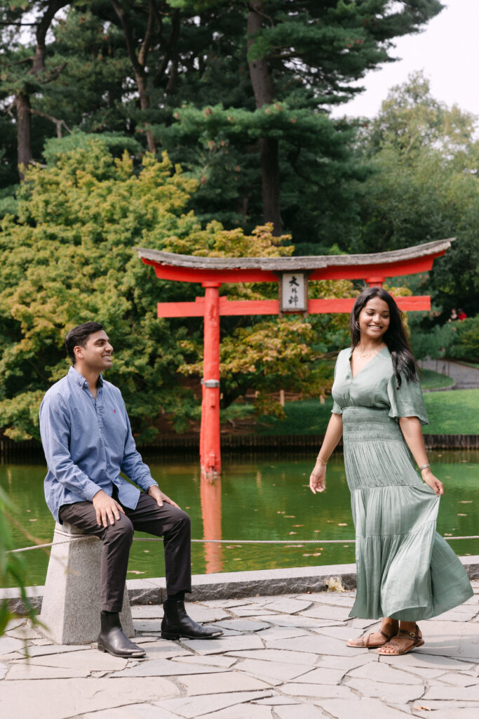 Playful candid engagement photo of a couple near the Japanese torii gate at Brooklyn Botanic Garden, captured by NYC proposal photographer.
