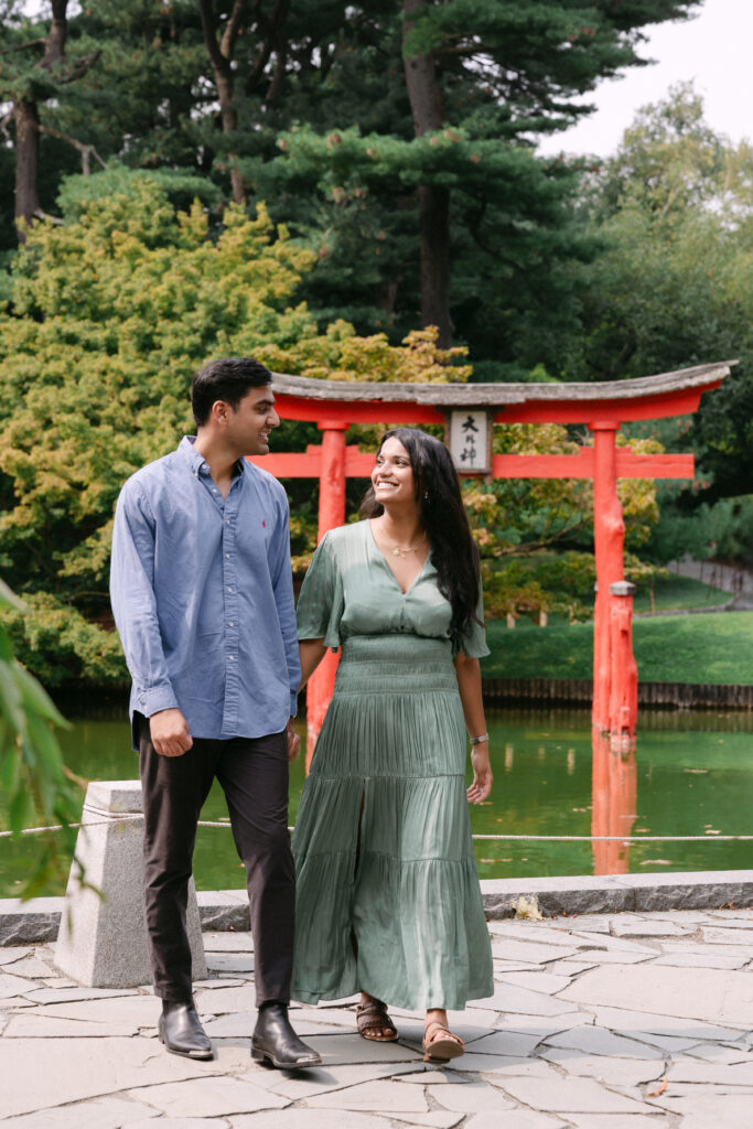 Engaged couple walking together near the Japanese torii gate at Brooklyn Botanic Garden, captured by NYC engagement and proposal photographer.
