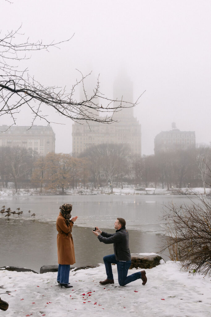 person kneeling to propose in foggy central park with snow and the manhattan skyline in the background