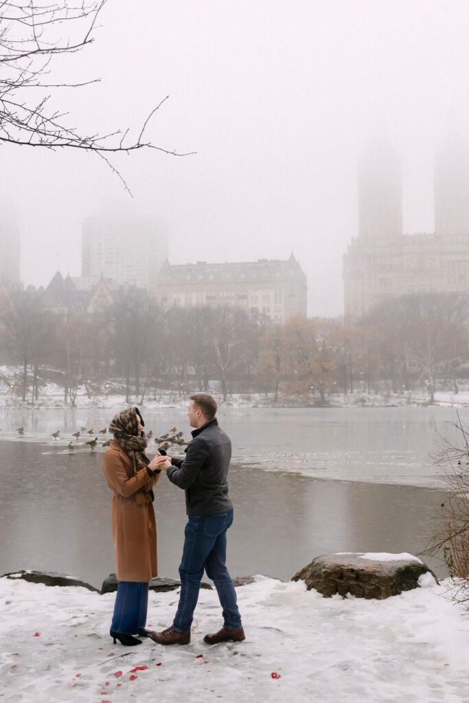 surprise proposal in foggy central park with snow and the manhattan skyline in the background