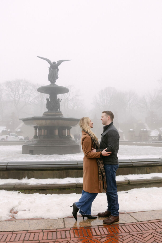 engaged couple standing together in front of bethesda fountain in central park on a foggy winter morning