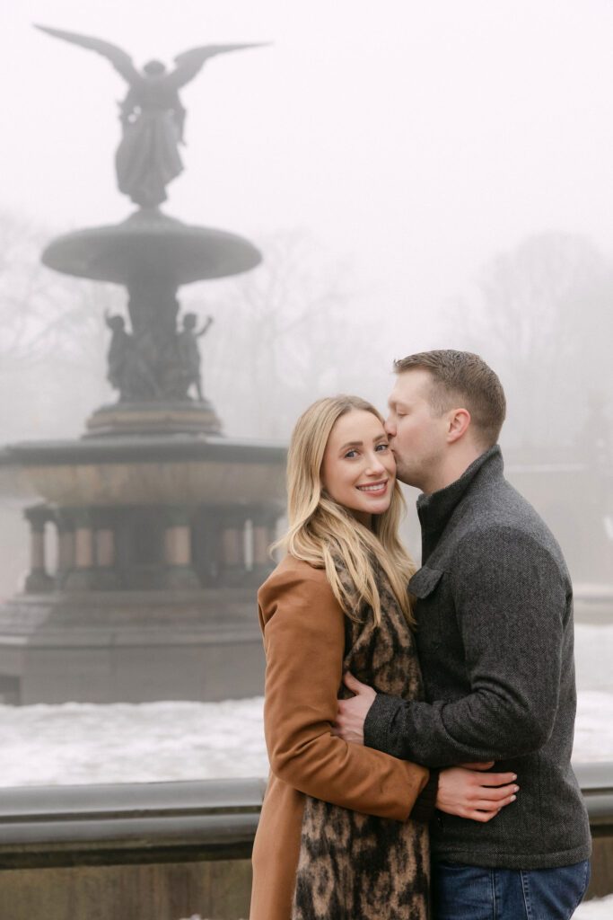 engaged couple hugging in front of bethesda fountain in central park on a foggy winter morning