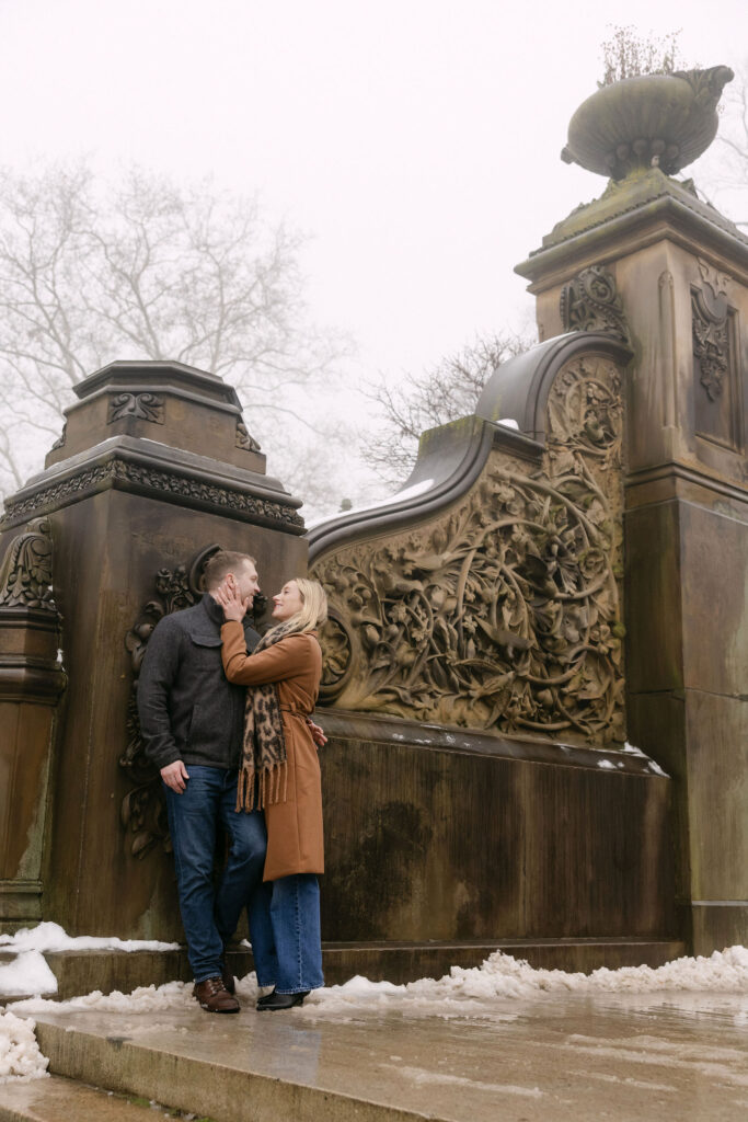 engaged couple standing on an ornate staircase in central park on a foggy winter morning