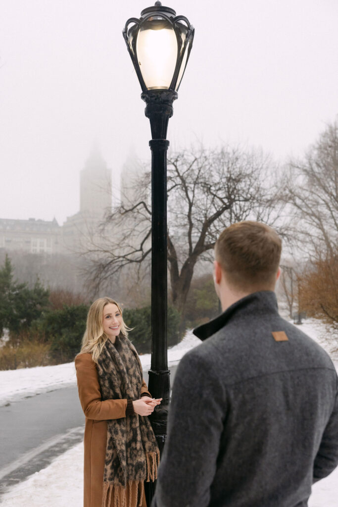 couple talking on a foggy winter path in central park near a lamppost after a surprise proposal