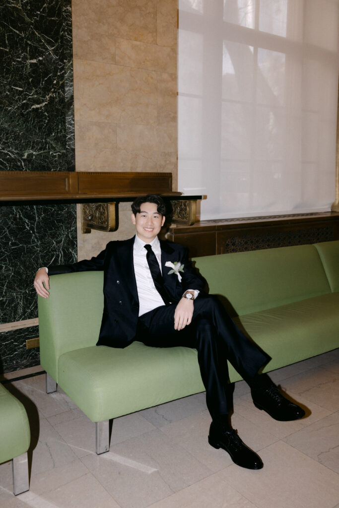 Groom sitting on a green bench inside NYC City Hall