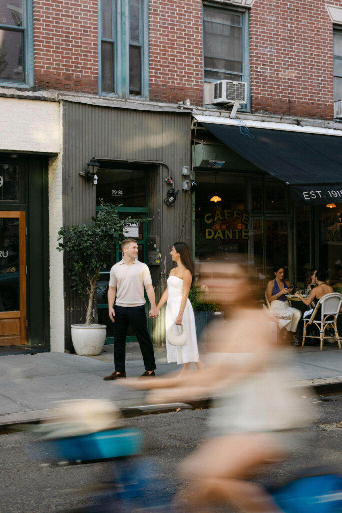 candid engagement photos of a couple standing on a west village sidewalk with motion blur from passing city traffic