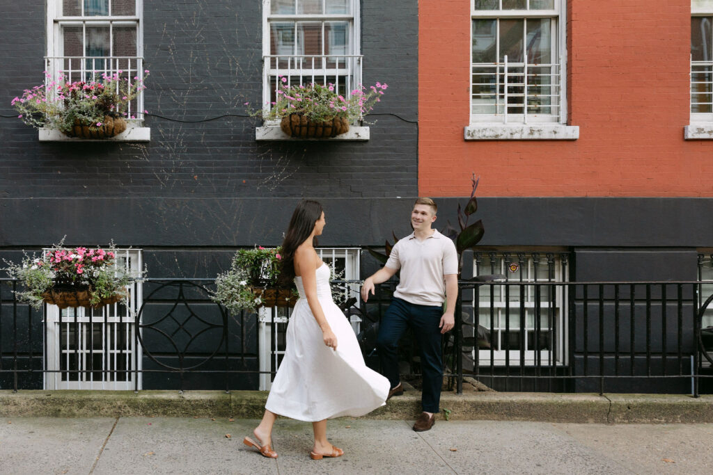 candid engagement photos of a couple walking past west village townhouses in new york city