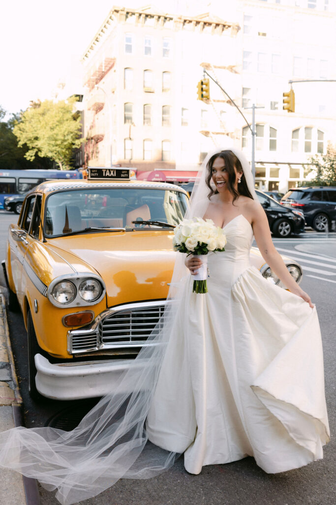 Bride holding a bouquet beside a vintage yellow taxi on a SoHo street during a New York City wedding photoshoot