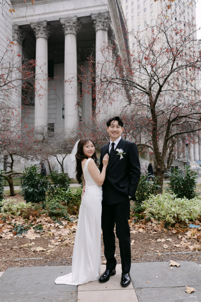 Bride and groom standing together in front of large stone columns