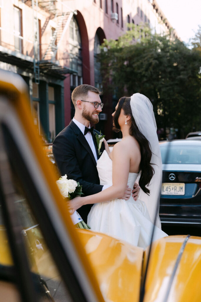 Bride and groom sharing a moment beside a yellow taxi on a SoHo street during a New York City wedding photoshoot