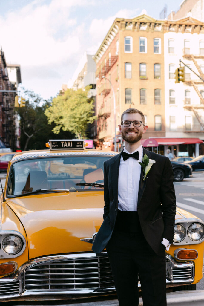 Groom standing next to a yellow taxi on a SoHo street in New York City on his wedding day