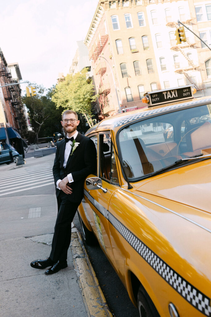 Groom standing beside a vintage yellow taxi on a SoHo street during a New York City wedding photoshoot