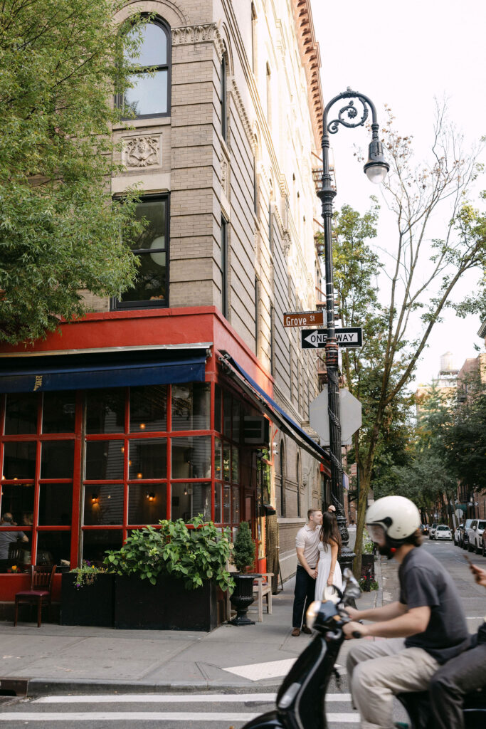 engagement photos of a couple pausing on a west village street corner with classic new york city buildings