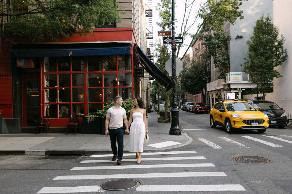 engagement photos of a couple crossing the street in the west village with a yellow taxi in new york city