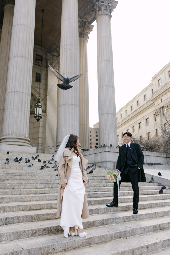 Couple standing on the steps of NYC City Hall framed by tall columns