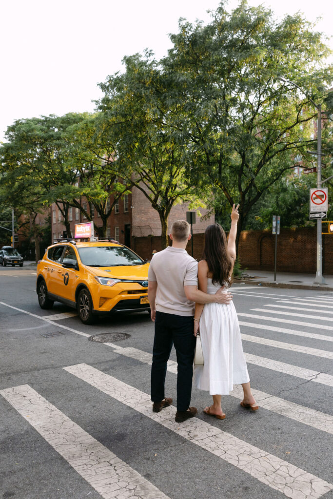 engagement photos of a couple standing at a crosswalk in the west village with a yellow taxi nearby