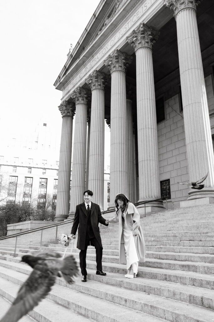 Couple walking down the wide steps of NYC City Hall with columns behind