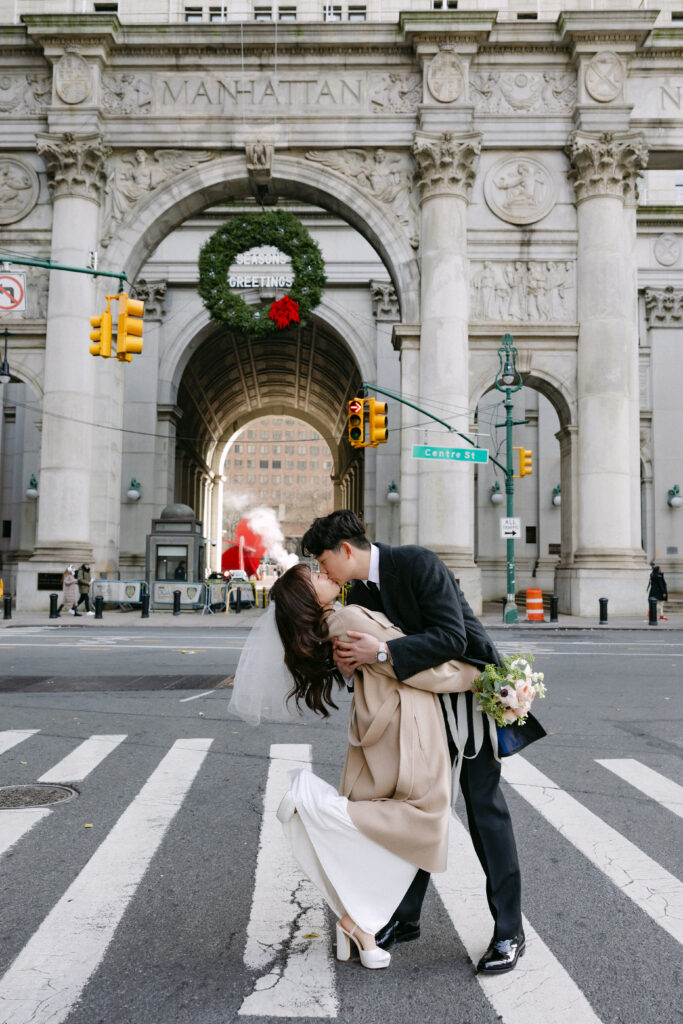 Bride and groom kissing in a city crosswalk with an arched building behind them