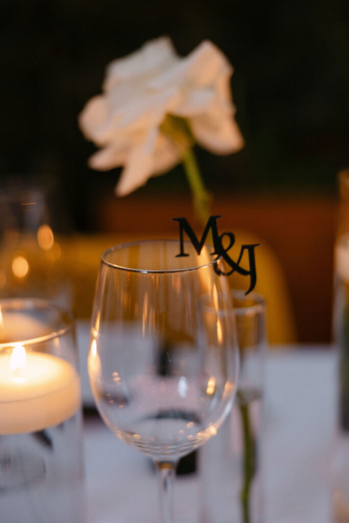 Personalized wedding reception place setting with custom monogram glassware, soft candlelight, and white florals at an intimate luxury New York City wedding.