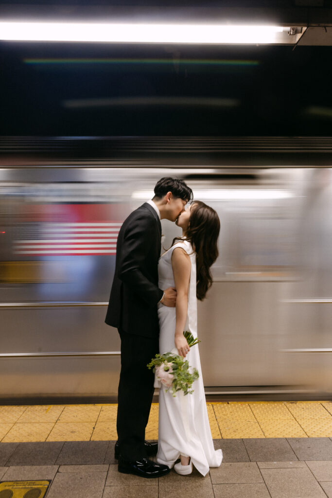Bride and groom kissing on a subway platform as a train passes