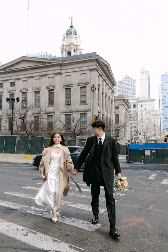 Bride and groom walking across the street near New York City Hall after their wedding
