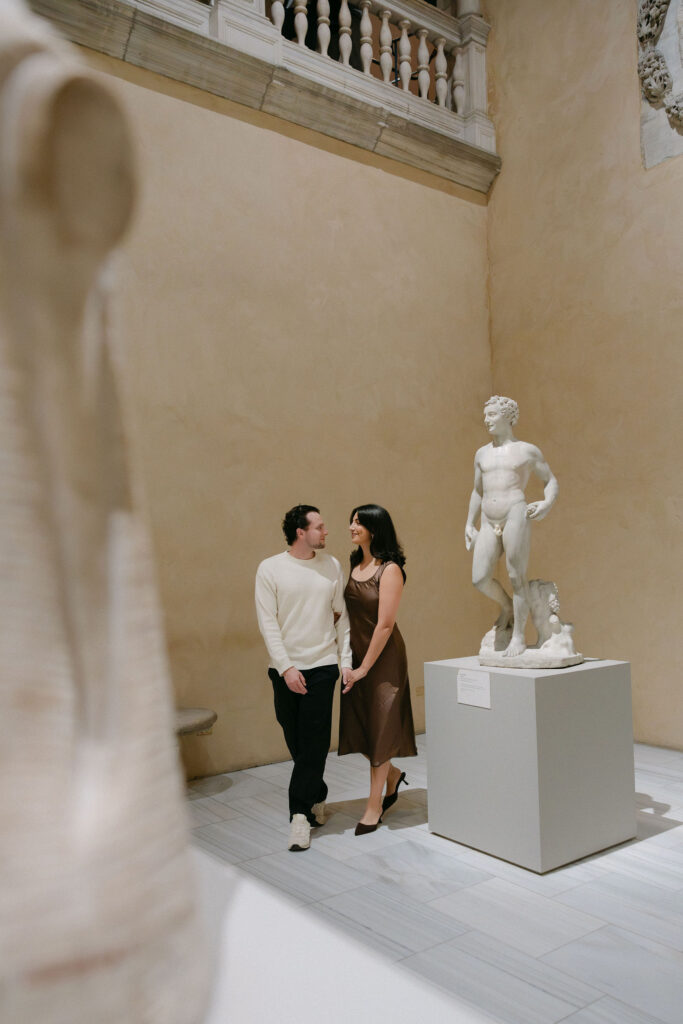 couple walking through a sculpture gallery at the metropolitan museum of art during an nyc engagement session