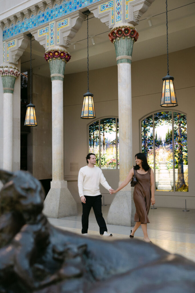 nyc engagement session photo of a couple walking together beneath historic columns near central park