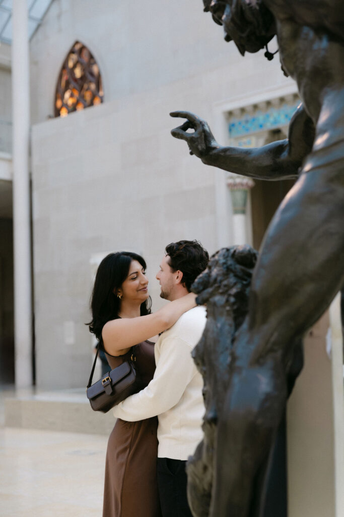 nyc engagement session photo of a couple sharing a close moment near a sculpture by central park