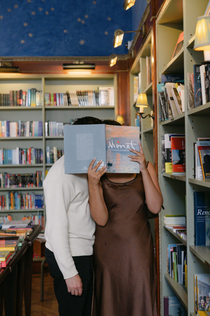 nyc engagement session photo of a couple playfully hiding behind a book inside a bookstore