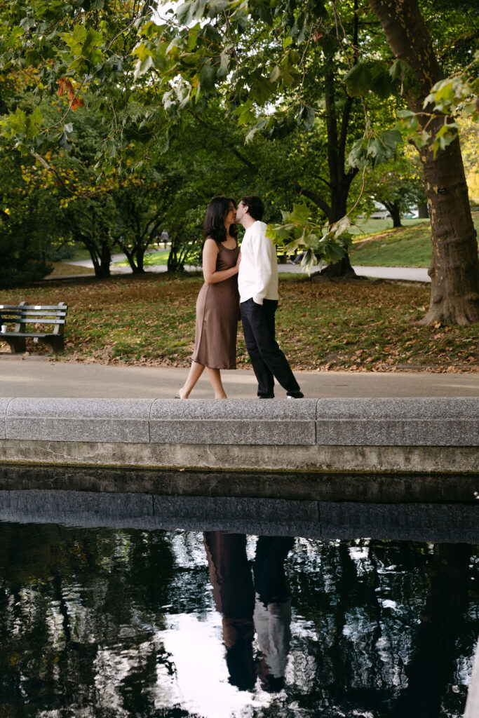 nyc engagement session photo of a couple walking beside a pond in central park