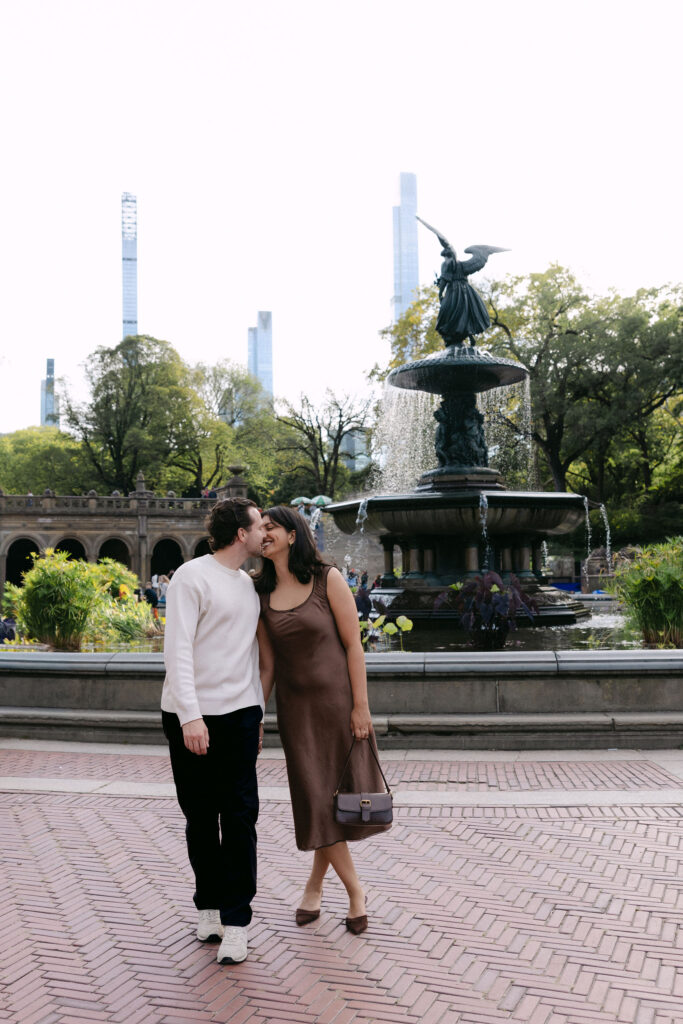 nyc engagement session photo of a couple walking together in central park near a fountain