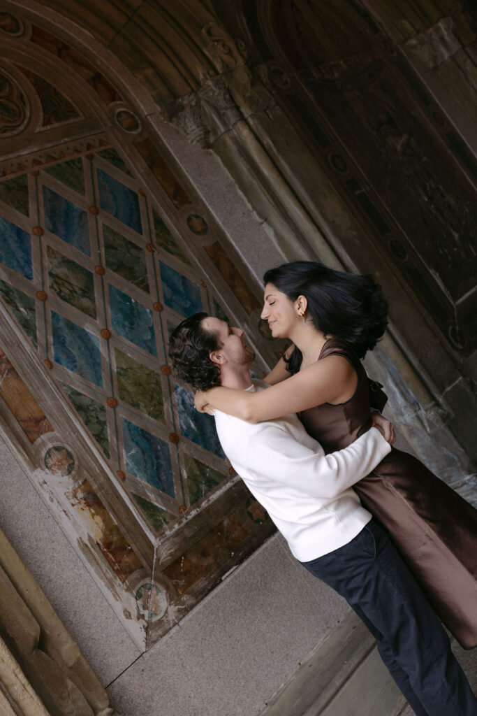 nyc engagement session photo of a couple embracing beneath an ornate archway in central park