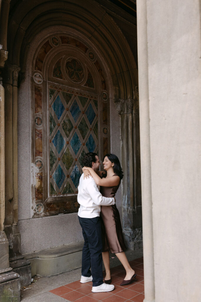 nyc engagement session photo of a couple standing together beneath a carved stone archway in central park