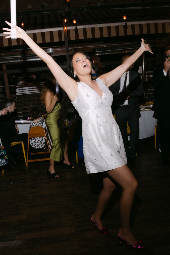 Bride celebrating with arms raised during a joyful late-night wedding reception in SoHo, New York City.
