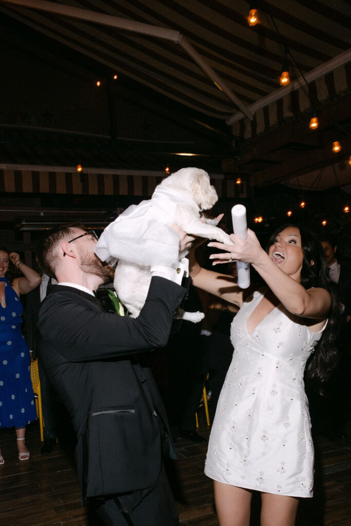 Bride and groom lifting their dog in the air during a joyful wedding reception in SoHo, New York City.
