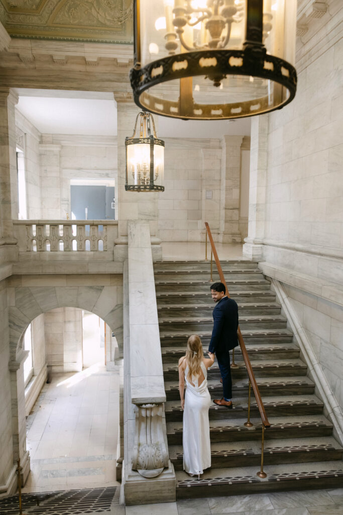 Couple standing on the grand staircase inside New York Public Library during romantic NYC engagement session
