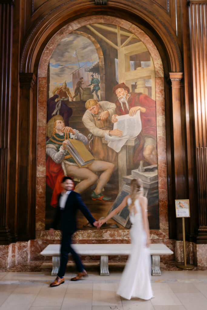 Couple dancing in front of historic mural inside New York Public Library during NYC engagement photos
