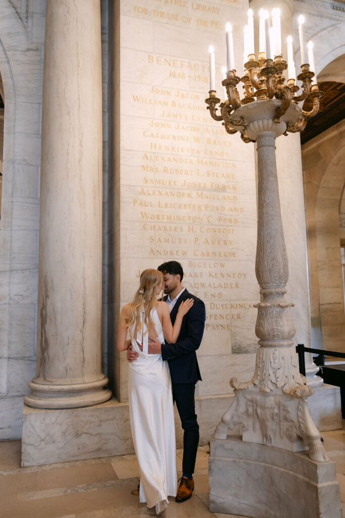 Couple embracing between columns inside New York Public Library during romantic NYC engagement photos