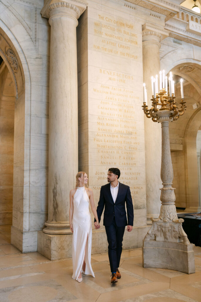 Couple walking through columns inside New York Public Library during romantic NYC engagement session