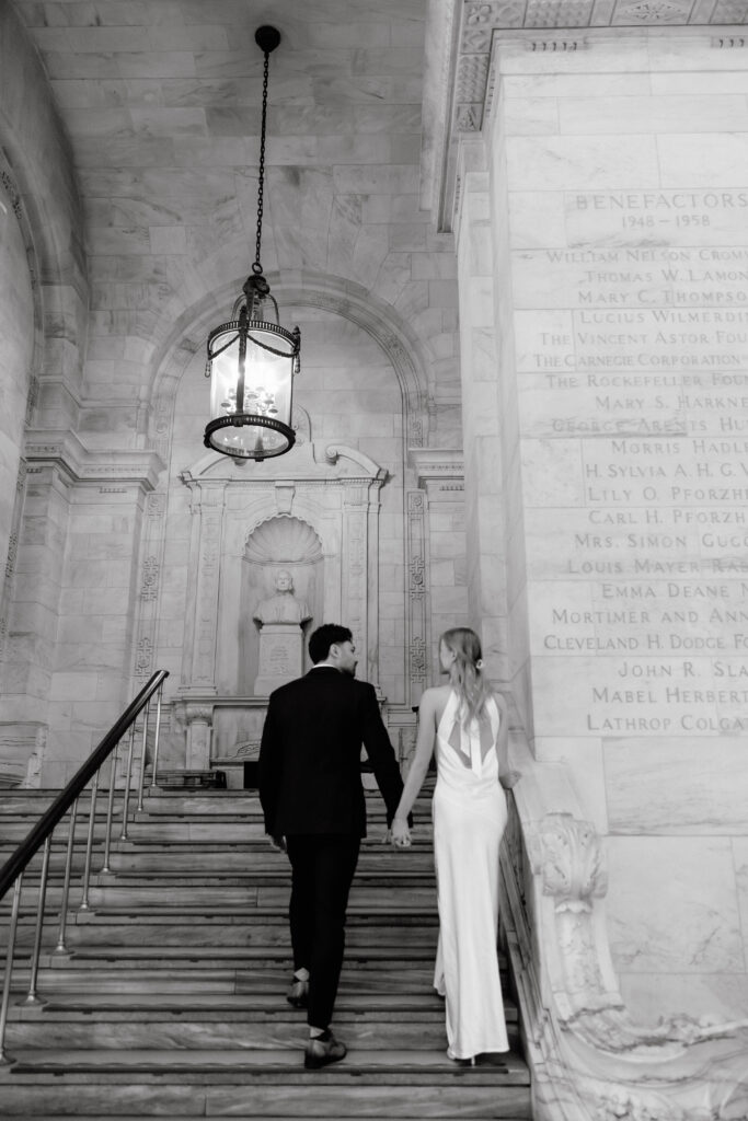 Black and white photo of couple walking up staircase inside New York Public Library during NYC engagement session