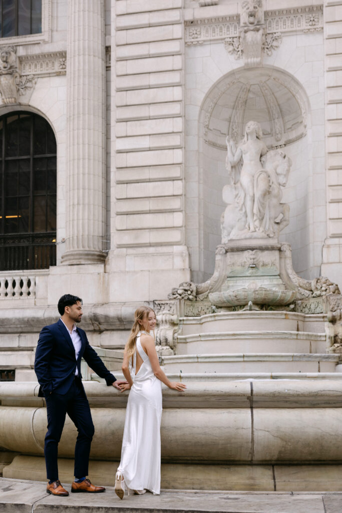 Couple walking outside New York Public Library near stone fountain during NYC engagement photos