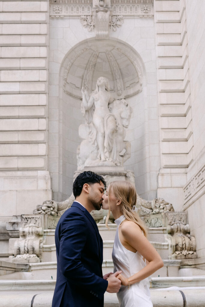 Couple embracing in front of fountain at New York Public Library during NYC engagement photos