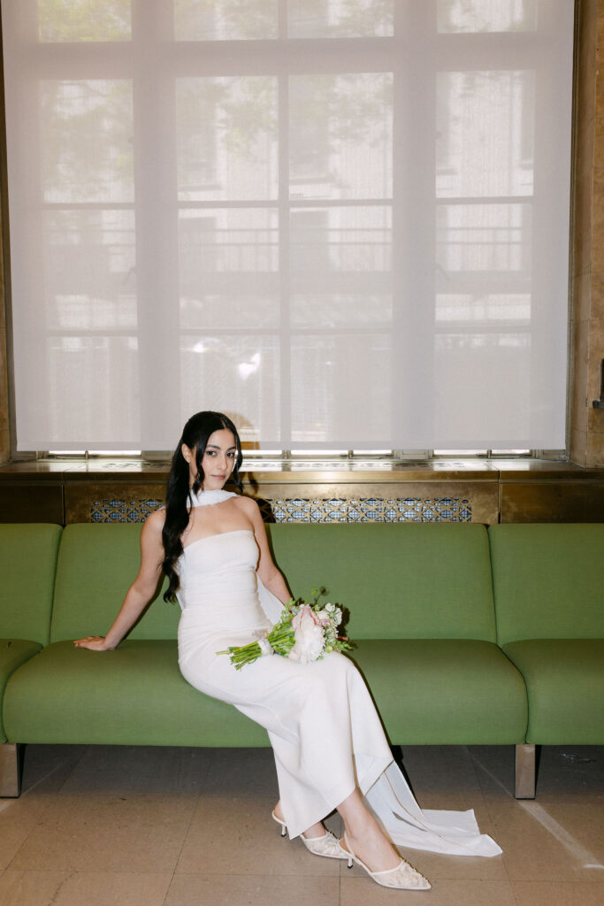 Bride sitting with her bouquet on the iconic green couch inside the Manhattan Marriage Bureau.