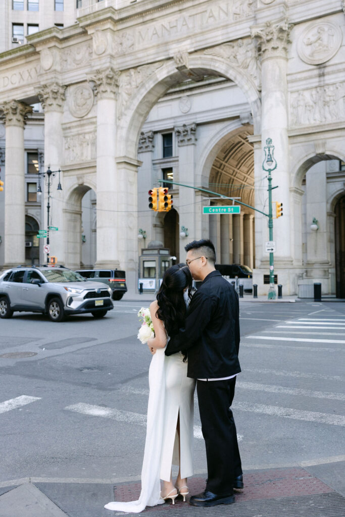 Newlyweds embracing near Centre Street with the Manhattan Municipal Building in the background after their City Hall wedding.