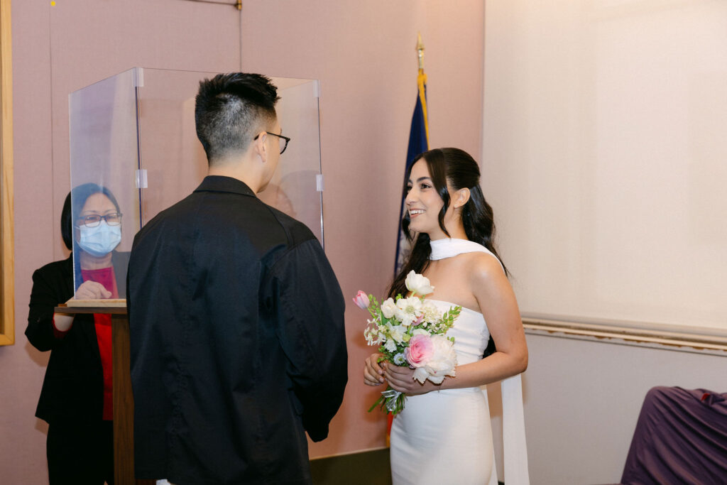 Bride smiling at the groom while holding her bouquet during their Manhattan City Hall wedding ceremony.