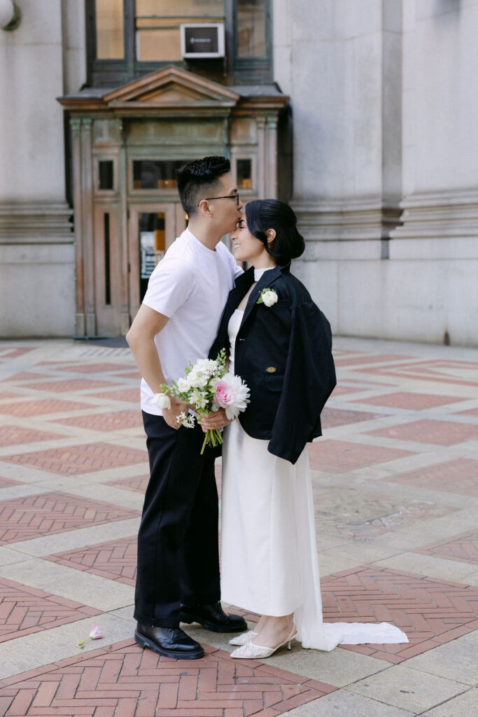 Groom kissing the bride on the forehead during their Manhattan City Hall wedding portraits in Lower Manhattan.