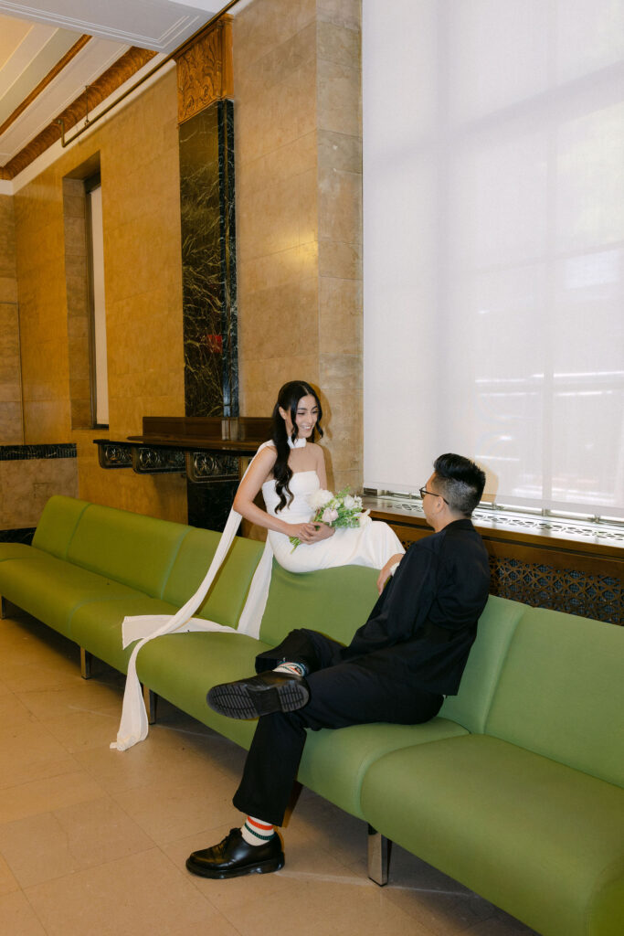 Bride and groom sitting across from each other on the green couches inside the Manhattan Marriage Bureau.