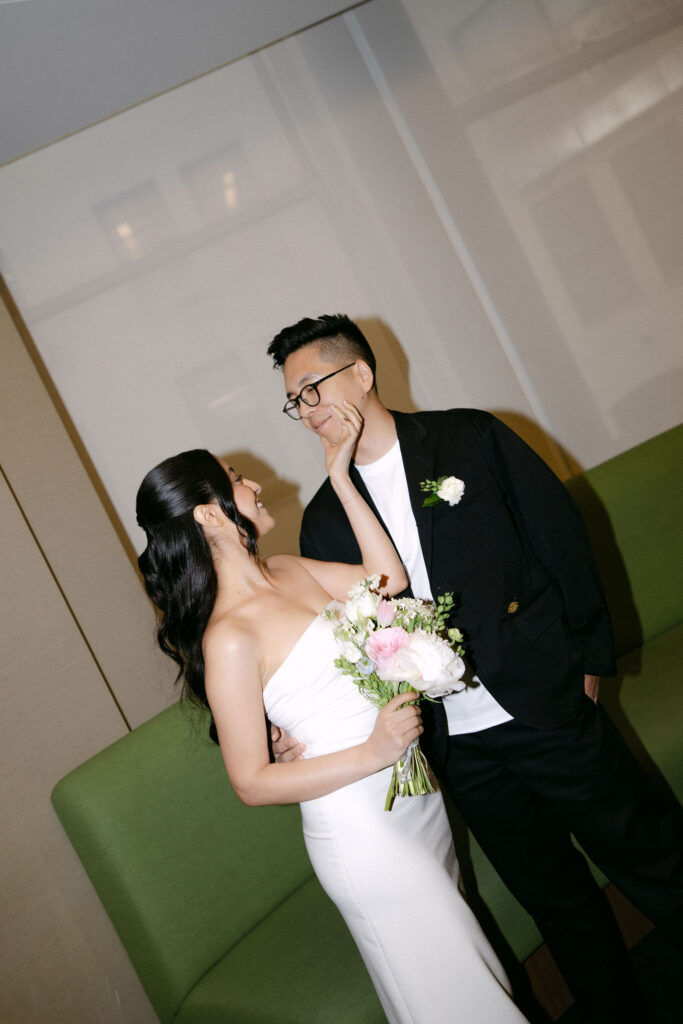 Newly married couple standing together beside the iconic green couch during their Manhattan City Hall wedding.