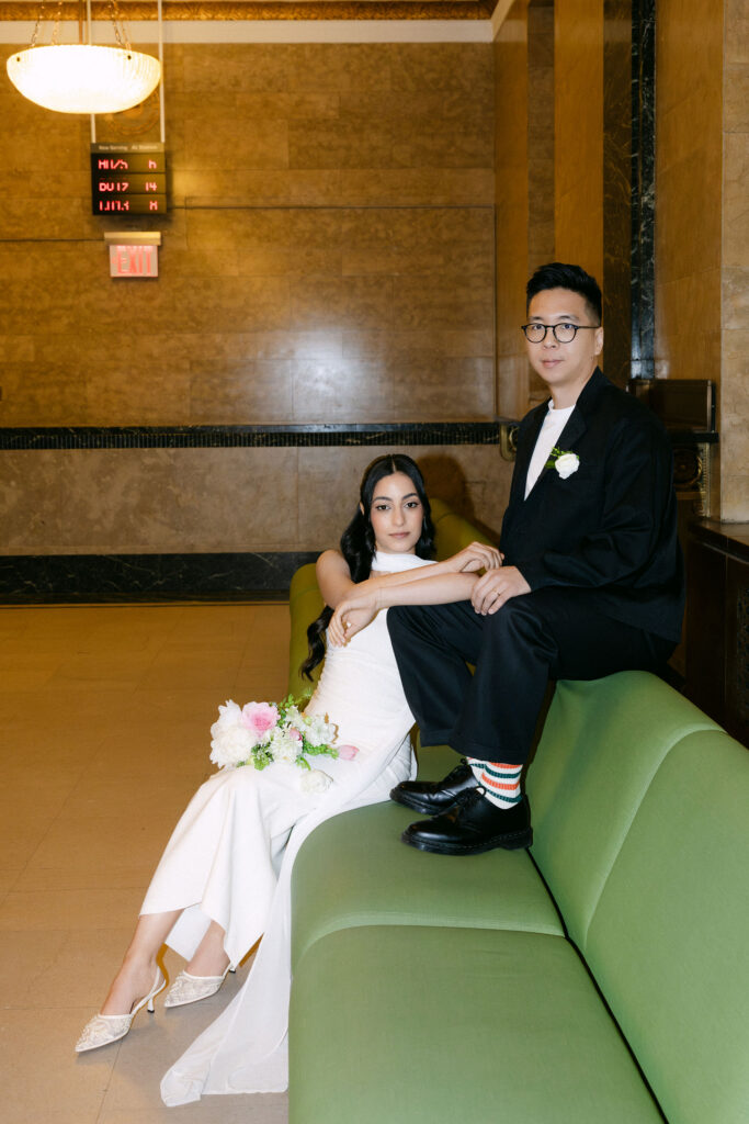 Bride and groom posing together on the green couch inside the Manhattan Marriage Bureau during their City Hall wedding.
